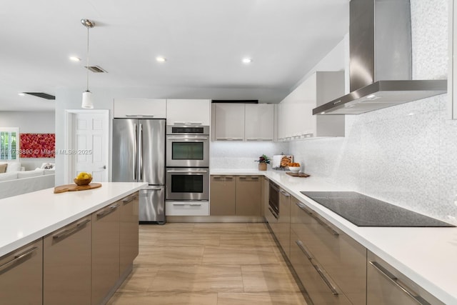 kitchen featuring stainless steel appliances, light countertops, wall chimney exhaust hood, modern cabinets, and decorative light fixtures