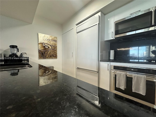 kitchen featuring appliances with stainless steel finishes, white cabinetry, dark stone countertops, and modern cabinets