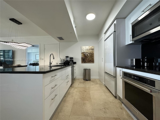 kitchen with white cabinets, dark countertops, stainless steel appliances, pendant lighting, and a sink