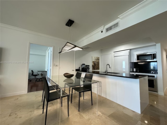 kitchen with crown molding, stainless steel appliances, dark countertops, visible vents, and a sink