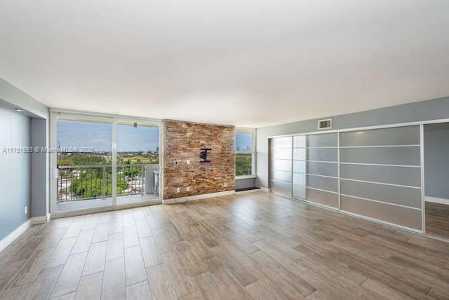 unfurnished living room featuring baseboards, visible vents, a wall of windows, and wood finished floors