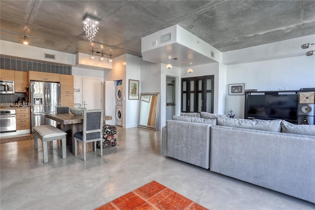 living area featuring concrete floors, stacked washing maching and dryer, and visible vents