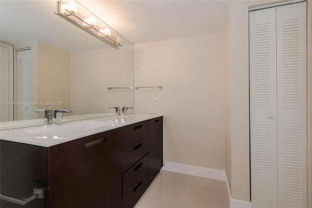 bathroom featuring double vanity, a closet, a sink, tile patterned flooring, and baseboards