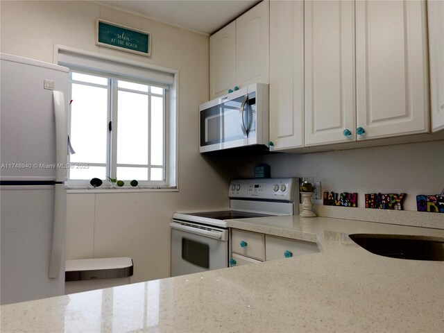 325 Ocean Dr Unit 308, Miami Beach, FL 33139 - kitchen with appliances with stainless steel finishes, white cabinets, a sink, and light stone counters