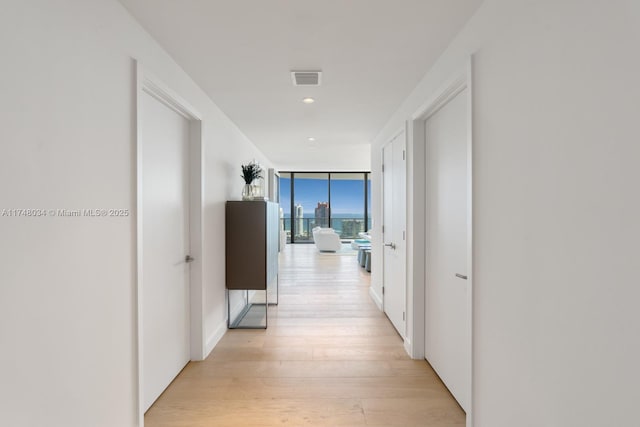 hallway with light wood-type flooring, floor to ceiling windows, and visible vents