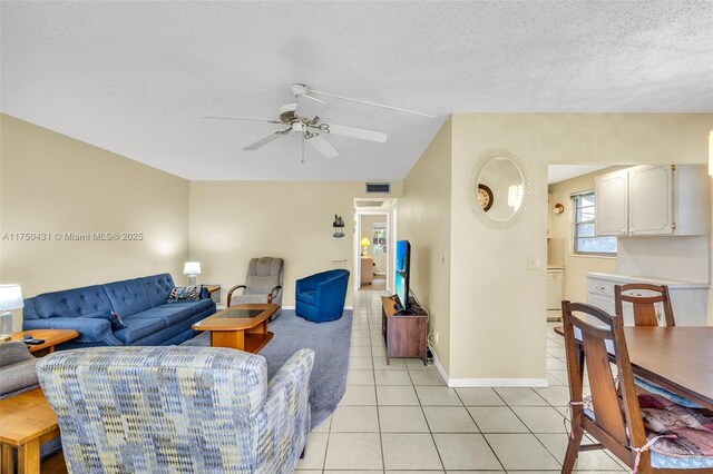 living room with baseboards, light tile patterned floors, a textured ceiling, visible vents, and ceiling fan