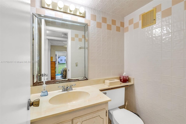 bathroom featuring vanity, visible vents, tile walls, and toilet