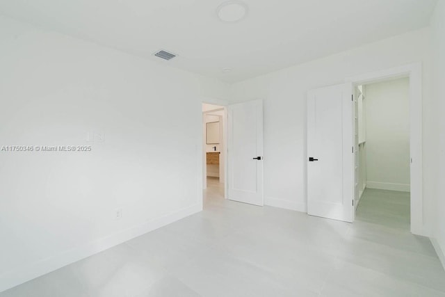 unfurnished bedroom with a walk in closet, visible vents, and baseboards