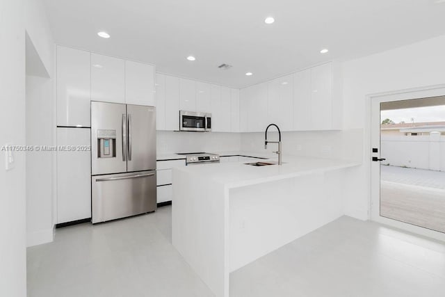 kitchen featuring stainless steel appliances, light countertops, white cabinets, a sink, and a peninsula