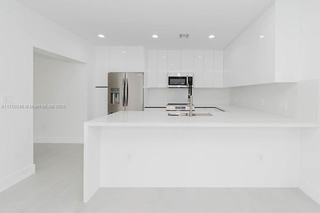 kitchen with modern cabinets, appliances with stainless steel finishes, a peninsula, light countertops, and white cabinetry