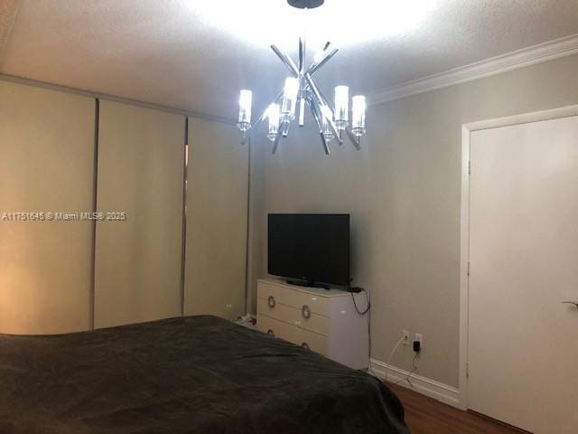 unfurnished bedroom featuring baseboards, ornamental molding, wood finished floors, and a notable chandelier