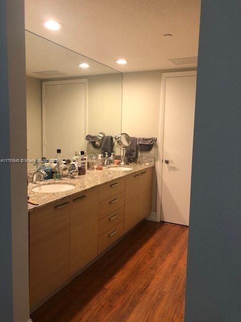 full bath featuring double vanity, wood finished floors, a sink, and recessed lighting