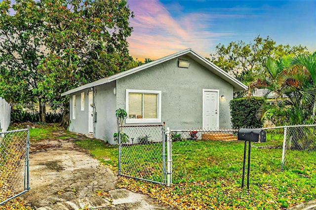 property exterior at dusk with a lawn, fence private yard, a gate, and stucco siding