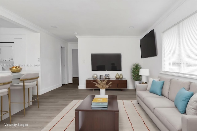 living room featuring baseboards, stacked washer and dryer, wood finished floors, and crown molding