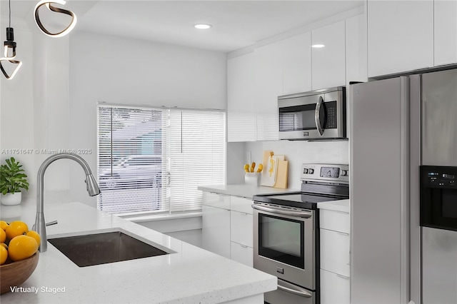 kitchen featuring pendant lighting, stainless steel appliances, white cabinets, a sink, and modern cabinets