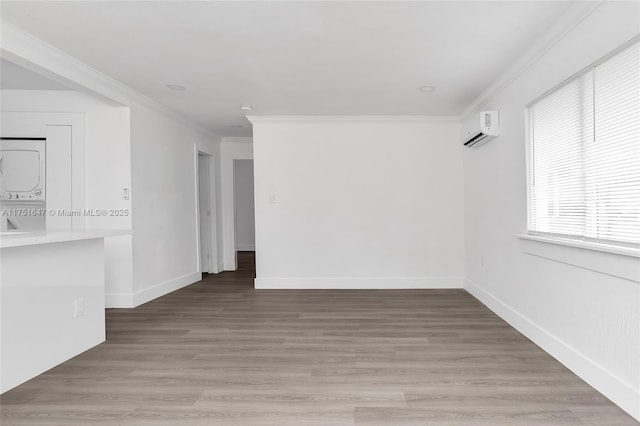 empty room with wood finished floors, crown molding, stacked washing maching and dryer, and a wall mounted AC