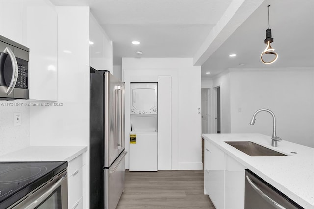 kitchen featuring hanging light fixtures, appliances with stainless steel finishes, stacked washer / dryer, white cabinets, and a sink