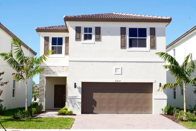 mediterranean / spanish-style house with stone siding, stucco siding, an attached garage, and driveway