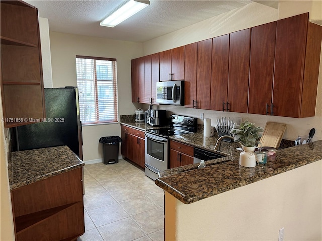 kitchen featuring dark stone countertops, a peninsula, stainless steel appliances, a textured ceiling, and open shelves