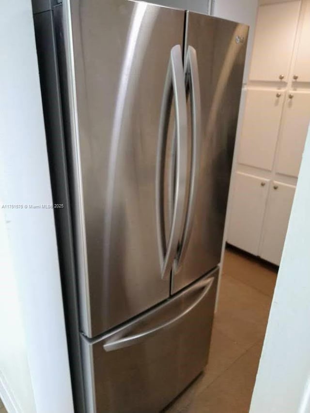 kitchen with light tile patterned floors, freestanding refrigerator, and white cabinets