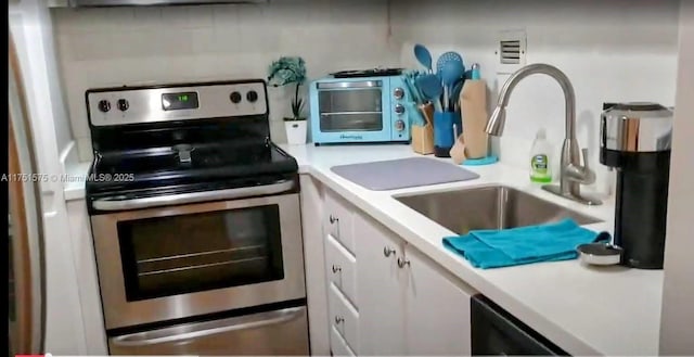 kitchen featuring stainless steel range with electric stovetop, a sink, light countertops, a toaster, and white cabinetry