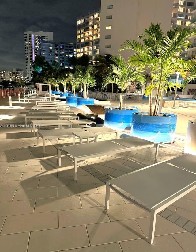 pool at night with a patio area, a view of city lights, and a pool