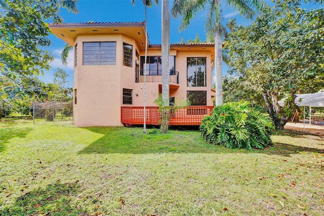 rear view of property featuring a lawn, a wooden deck, and stucco siding