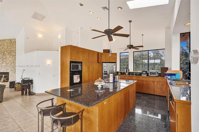 kitchen featuring brown cabinetry, a sink, a towering ceiling, and stainless steel fridge with ice dispenser