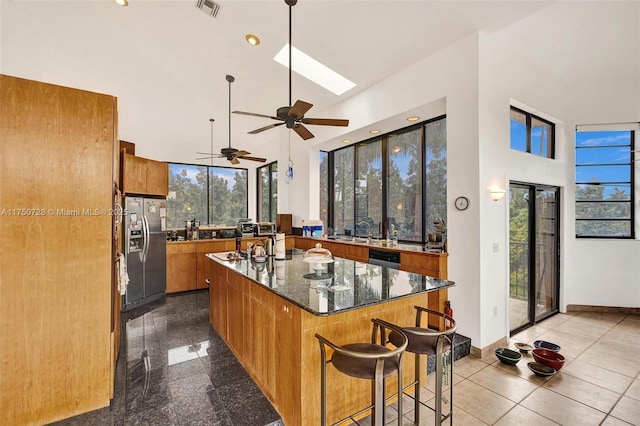 kitchen with high vaulted ceiling, stainless steel appliances, granite finish floor, a skylight, and brown cabinets