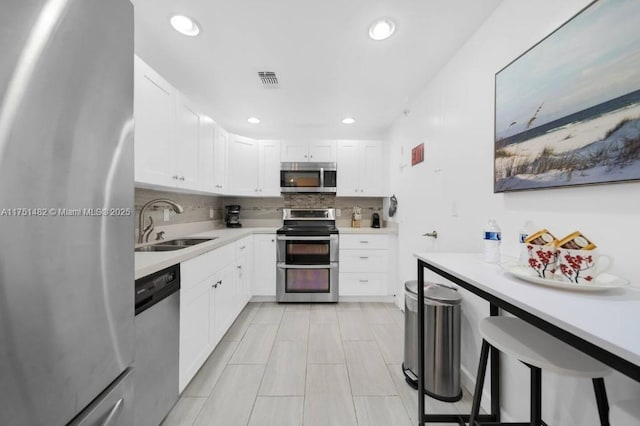 kitchen with tasteful backsplash, appliances with stainless steel finishes, light countertops, white cabinetry, and a sink