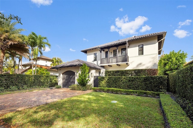 mediterranean / spanish home featuring decorative driveway, stucco siding, a balcony, a garage, and a front lawn