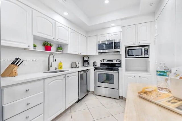 kitchen with appliances with stainless steel finishes, light countertops, white cabinetry, open shelves, and a sink