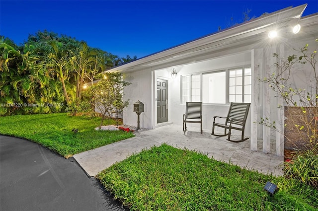 view of exterior entry featuring a lawn and stucco siding