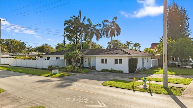 ranch-style house featuring stucco siding, fence, a front lawn, and a tiled roof