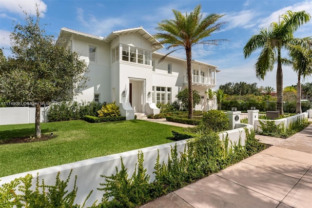 view of front of home featuring a balcony, stucco siding, a fenced front yard, and a front yard