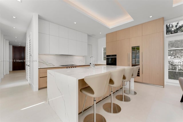 kitchen featuring backsplash, a sink, modern cabinets, oven, and a kitchen bar