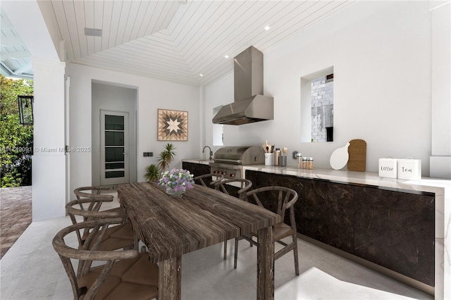 kitchen featuring wooden ceiling, wall chimney range hood, a sink, and ornate columns