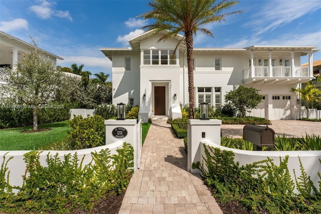 view of front facade with a fenced front yard, decorative driveway, stucco siding, an attached garage, and a balcony