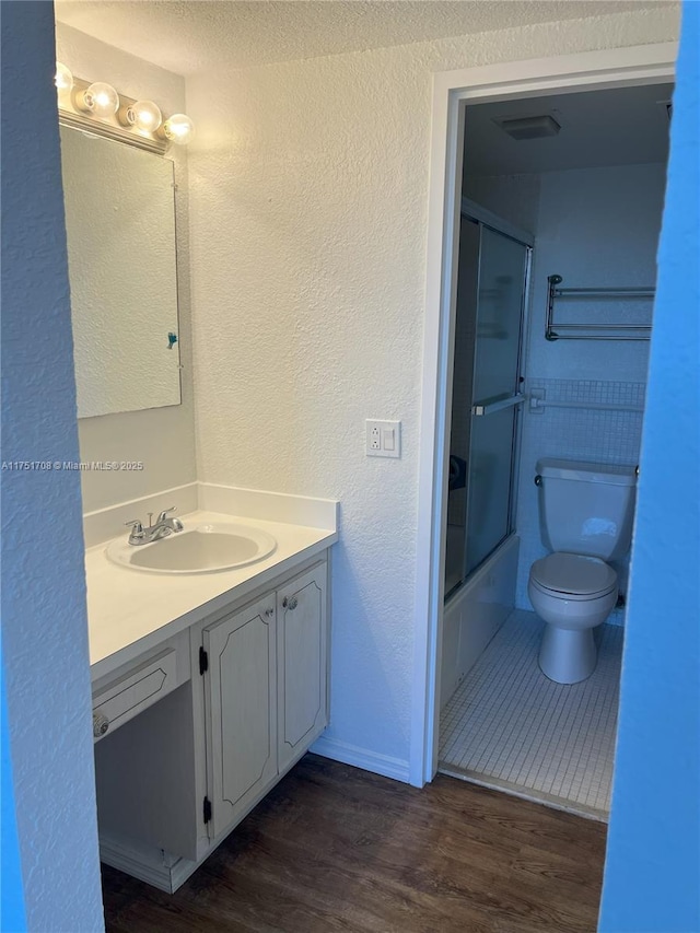 3660 NE 166th St Unit 305, North Miami Beach, FL 33160 - bathroom with vanity, wood finished floors, toilet, a textured wall, and bath / shower combo with glass door