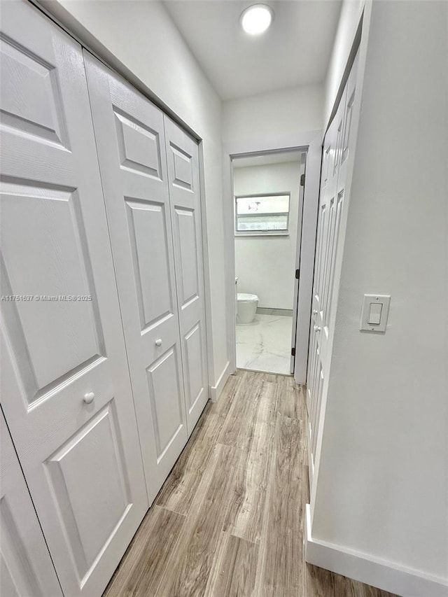 hallway featuring light wood finished floors and baseboards