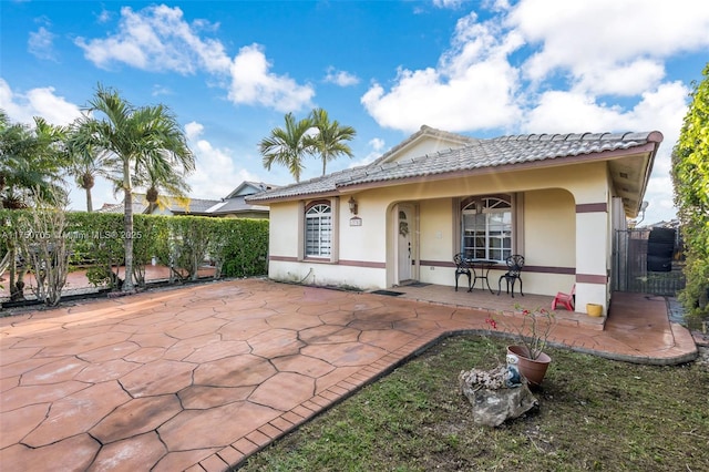 rear view of house with a patio area, fence, a tile roof, and stucco siding