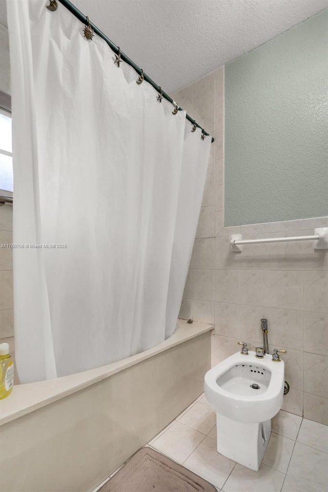 bathroom featuring a textured ceiling, tile patterned flooring, shower / tub combo, tile walls, and a bidet