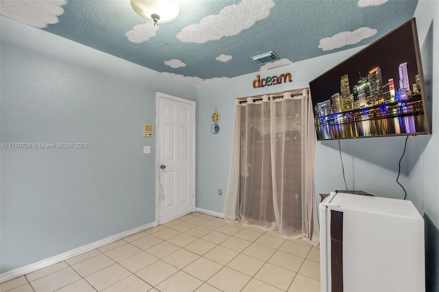 interior space with a textured ceiling, light tile patterned flooring, visible vents, and baseboards