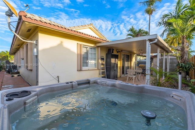 exterior space featuring a hot tub, a tiled roof, fence, and stucco siding