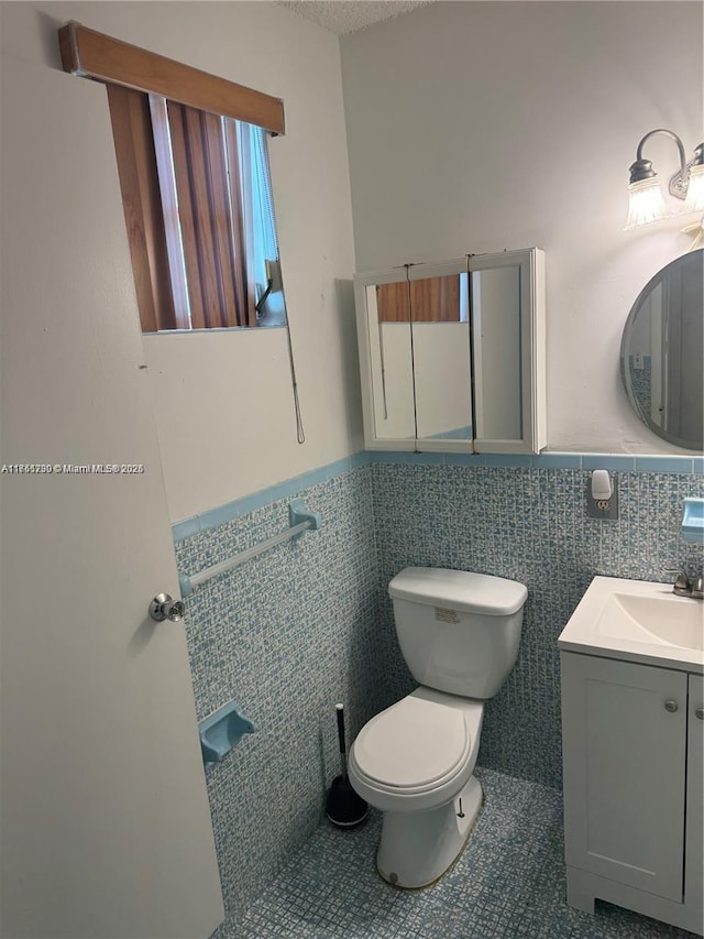 half bath with tile walls, a wainscoted wall, vanity, and toilet