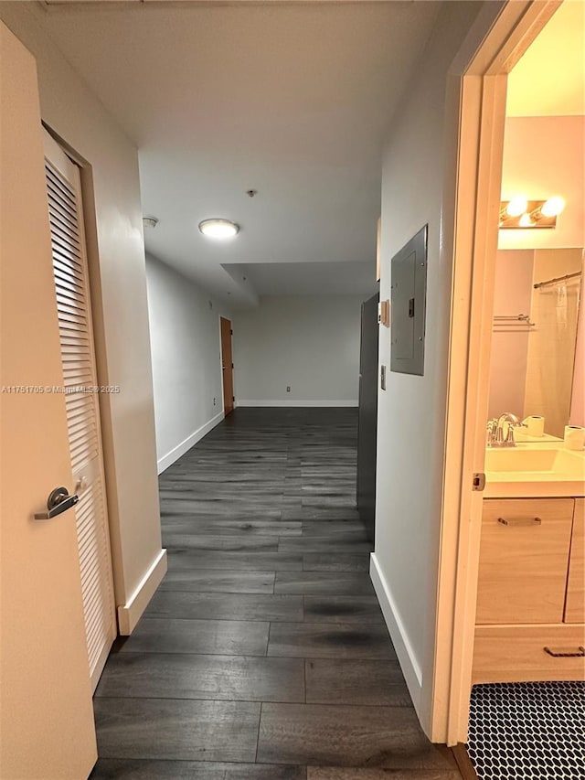 hall featuring dark wood finished floors, a sink, electric panel, and baseboards