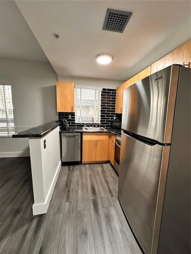 kitchen with stainless steel appliances, dark countertops, visible vents, a sink, and a peninsula