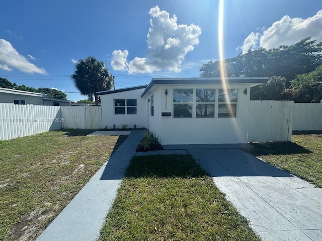 view of front of property with a front lawn, driveway, stucco siding, and fence
