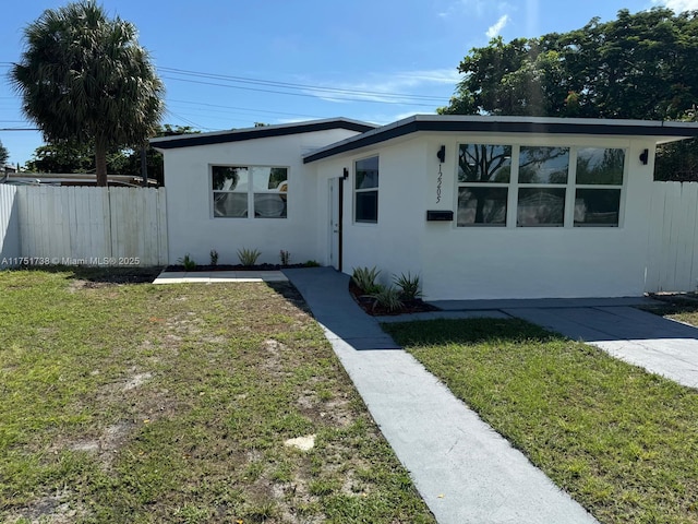 mid-century modern home featuring a front yard, stucco siding, and fence