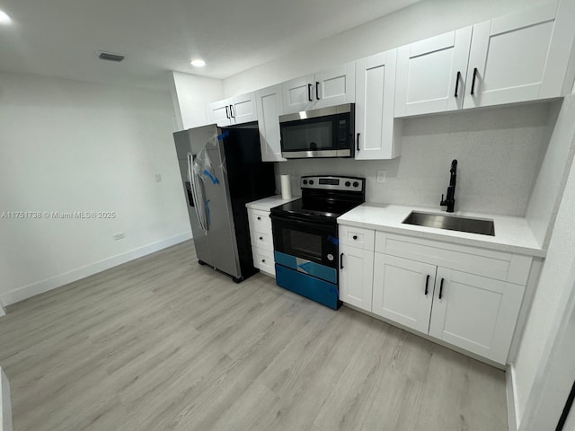 kitchen with light countertops, a sink, light wood-style flooring, stainless steel appliances, and baseboards